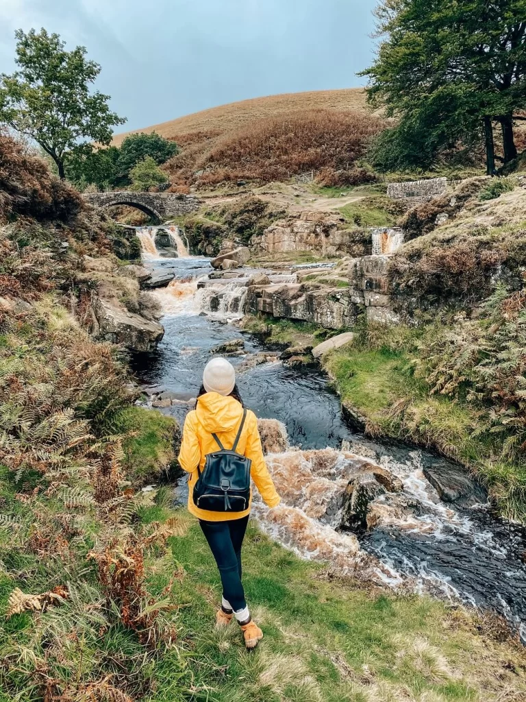 Female hiker in yellow jacket standing in front of a small waterfall