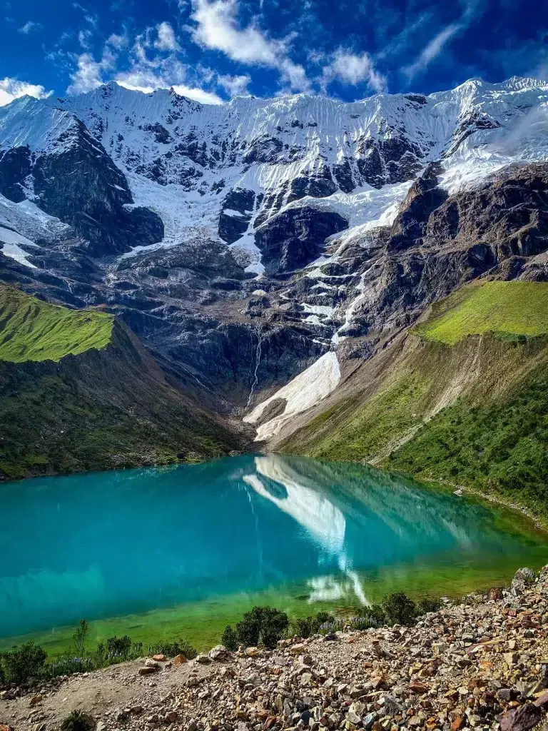 An image of snow capped mountain peak with an emerald lagoon on front of it
