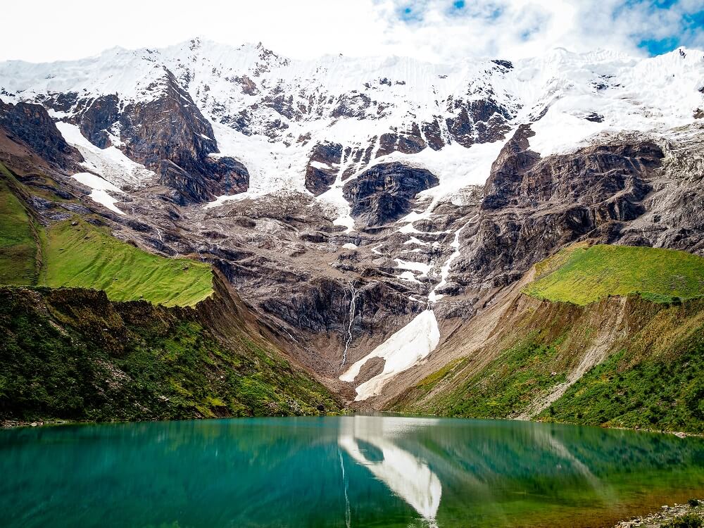 An image of snow capped mountain peak with an emerald lagoon on front of it