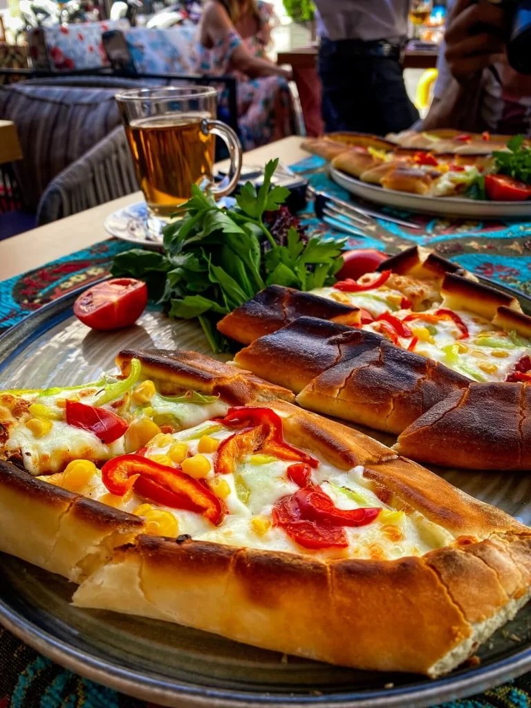 A pizza-like dish on a table called pide with cheese and pepper toppings