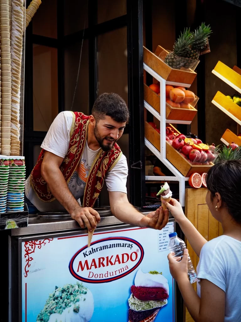 A male dressed in traditional Turkish vest giving ice cream to a young girl