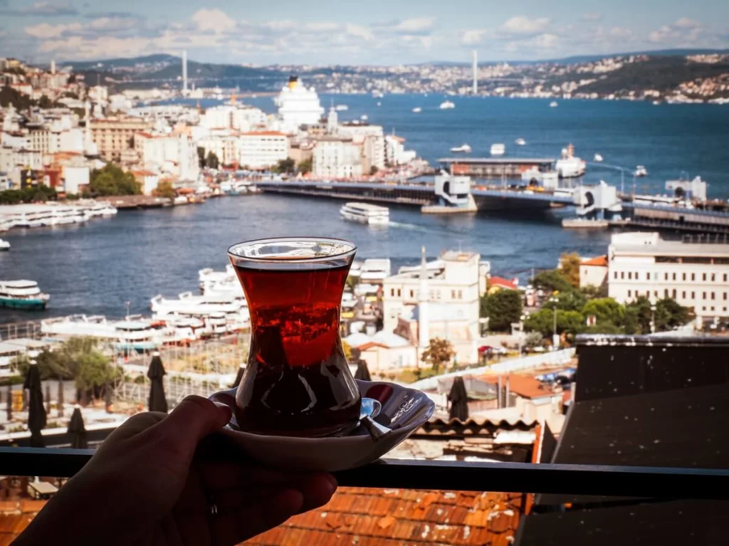 A hand is holding a glass of traditional Turkish tea with a view of the Bosporus Strait in Istanbul 