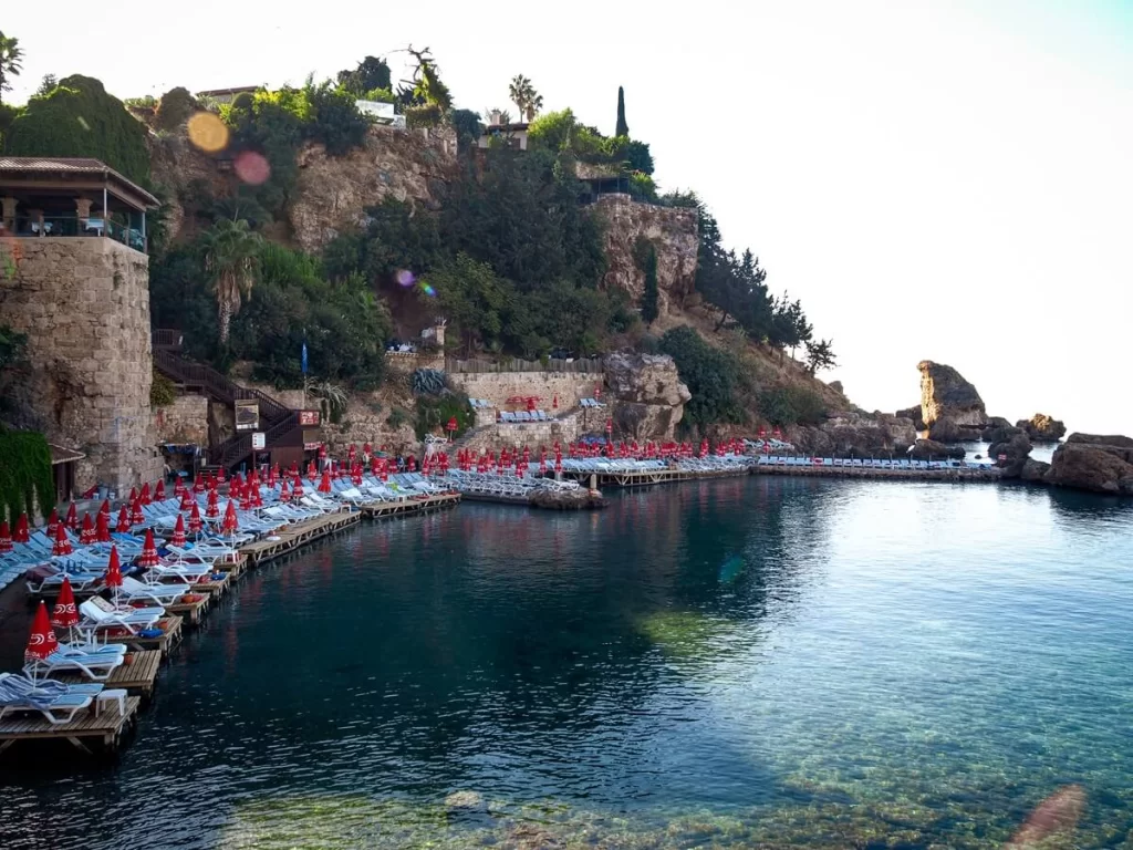 blue beach beds and red umbrellas arranged in a semi circle in the side of a cliff in front of the sea
