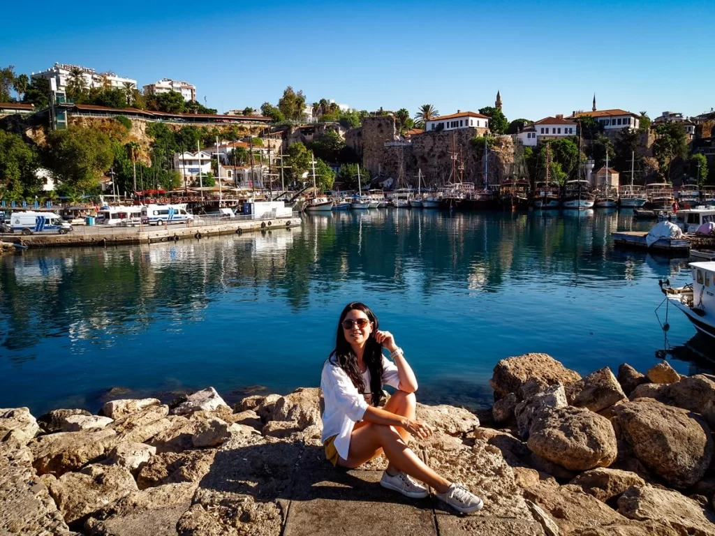 A female traveller is sitting on a rock in front of a harbour
