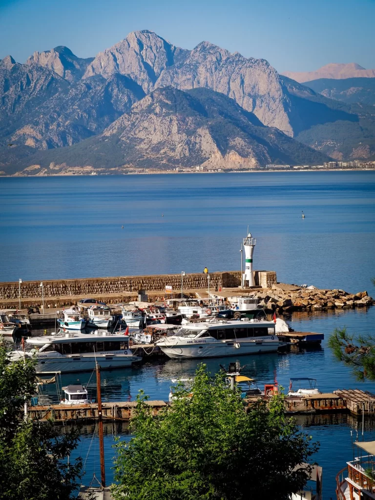 Antalya harbour with boats docked in front of a lighthouse and mountains in the background