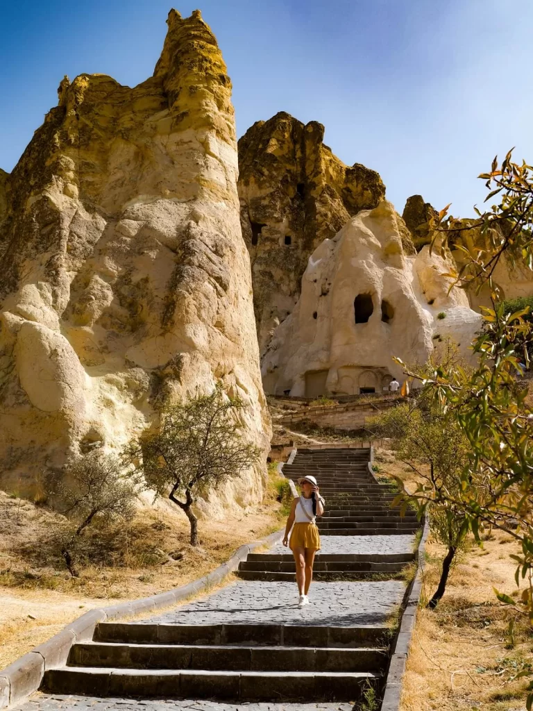 A female traveller is walking down the steps next to some tall rock formations in Cappadocia Turkey