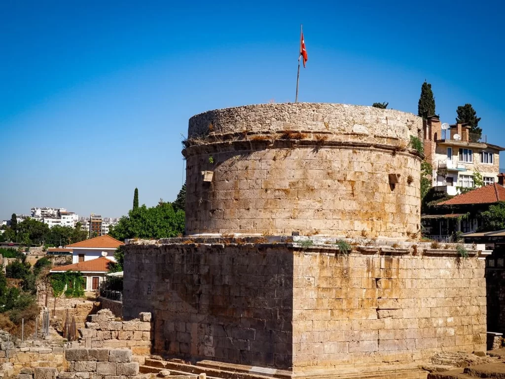 An old tower building with a square bottom and a round top half with a Turkish flag on top