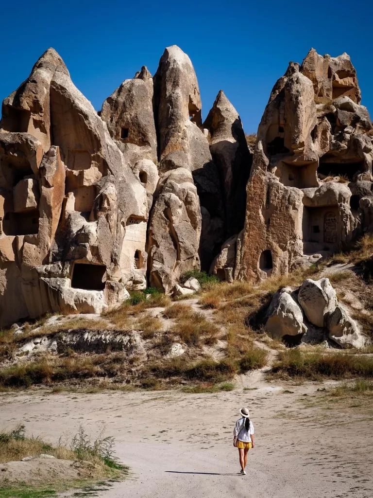 Female hiker walking along a wide dirt path towards some rock formations in Cappadocia Turkey