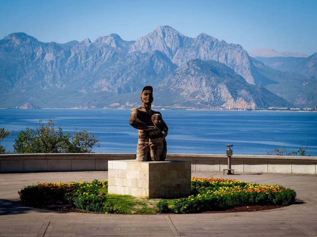 A statue of two people on a square block with sea and mountain views in the background