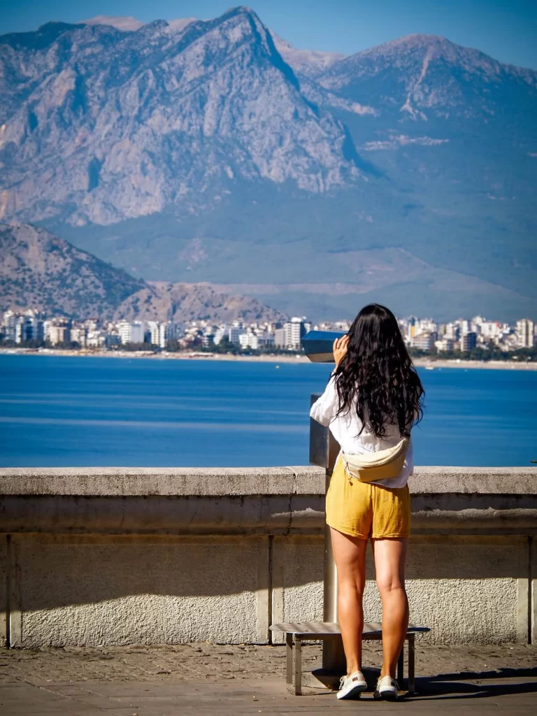 A female traveller is standing at a viewpoint looking out to the sea and mountains
