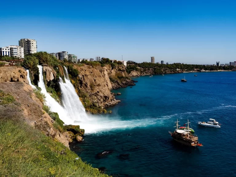 Waterfall cascading into the sea from a cliff with tourist boats around it in Antalya Turkey