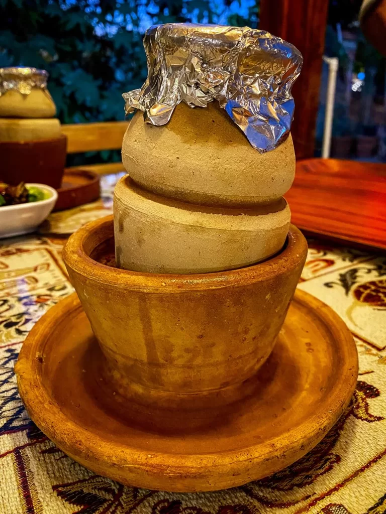 A clay pot on a table covered with foil which has traditional Turkish food in it