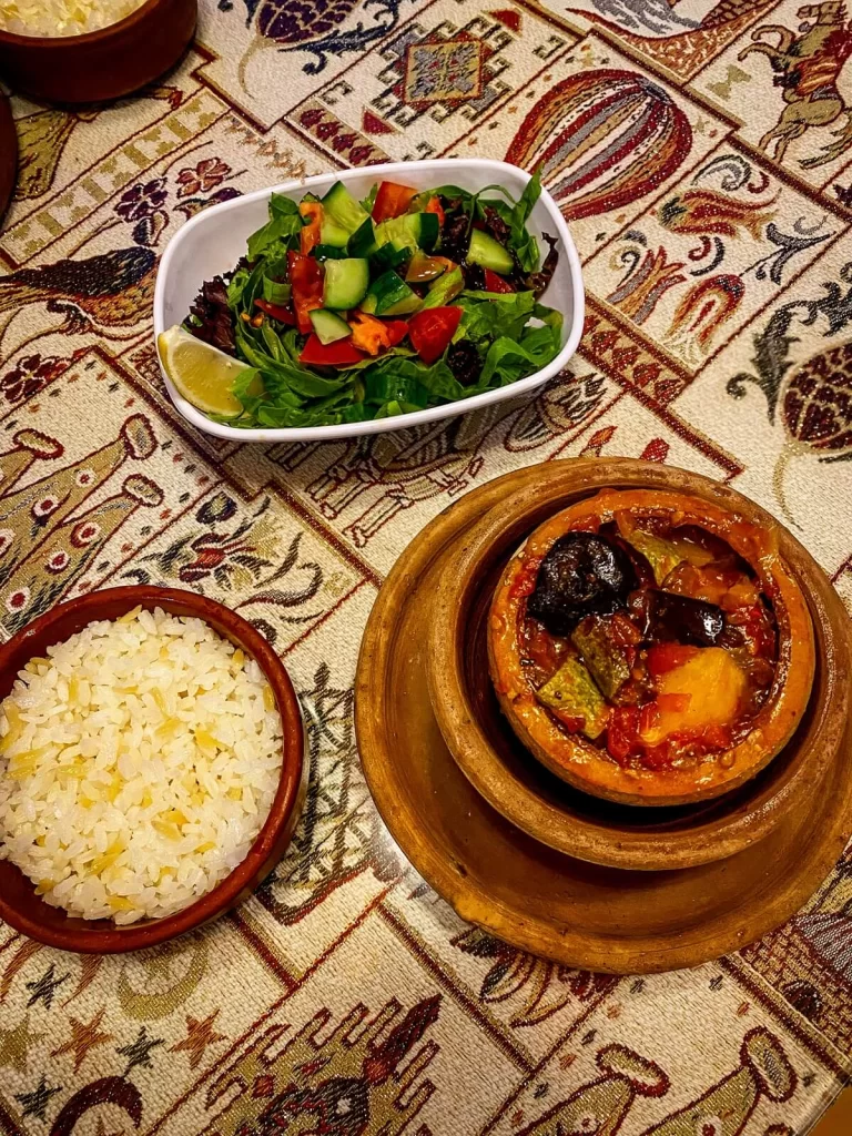 a table with an embroidered table cloth, one rice, one salad and a vegetable stew dish in a clay pot