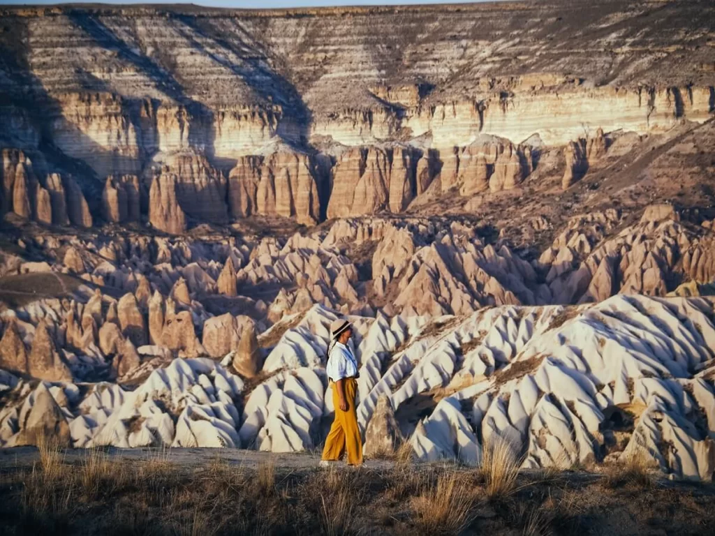 A female traveller is walking along a path in front of rock formations during golden hour