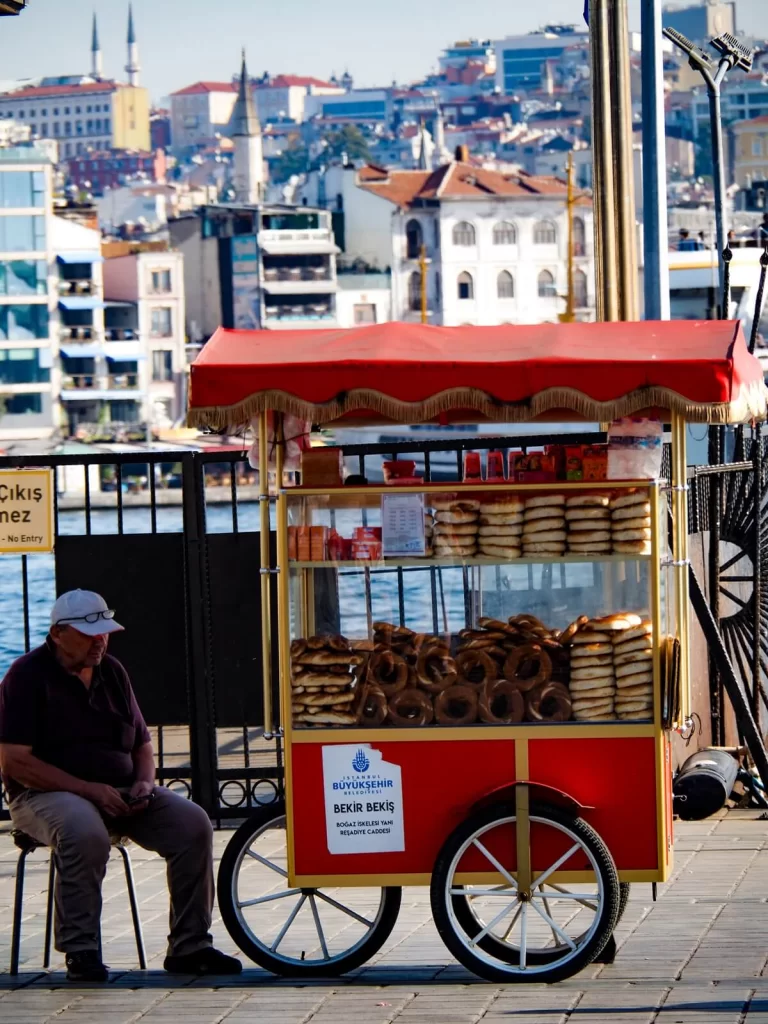 A street food vendor is sitting next to a red street food cart selling simit in Istanbul