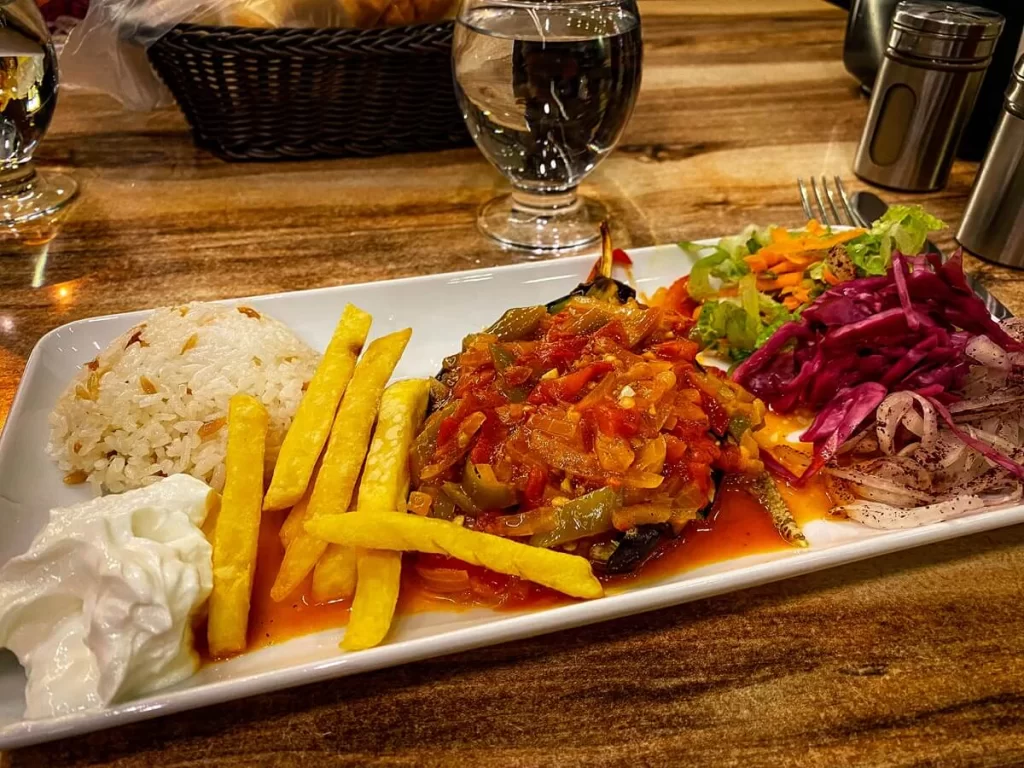 a plate with rice, sauce, fries, aubergine and salad