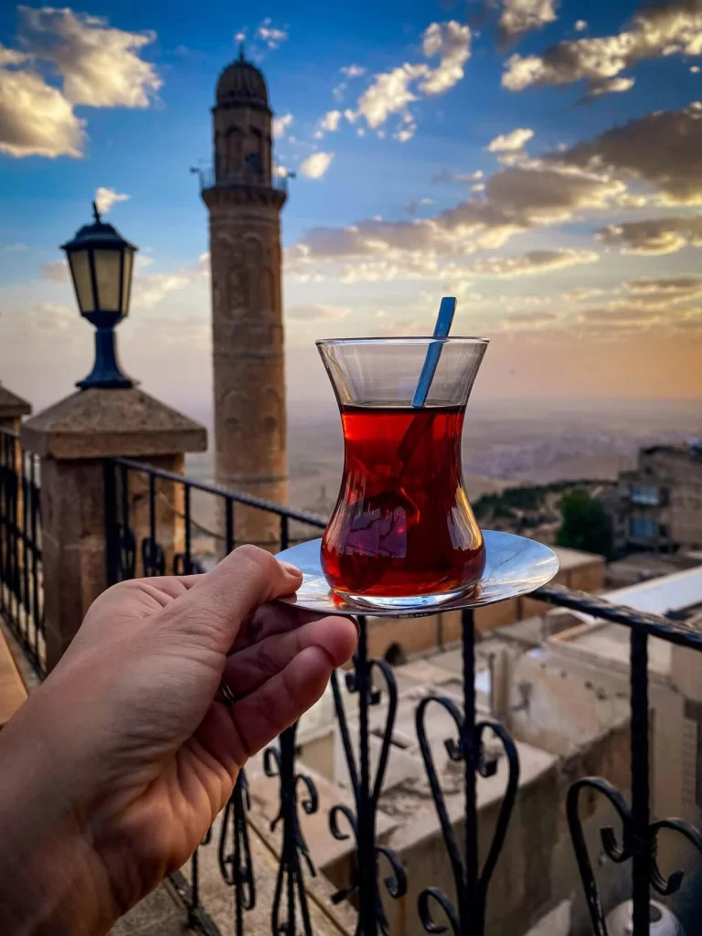 A female hand is holding a glass of traditional Turkish tea during sunset with a minaret in the background