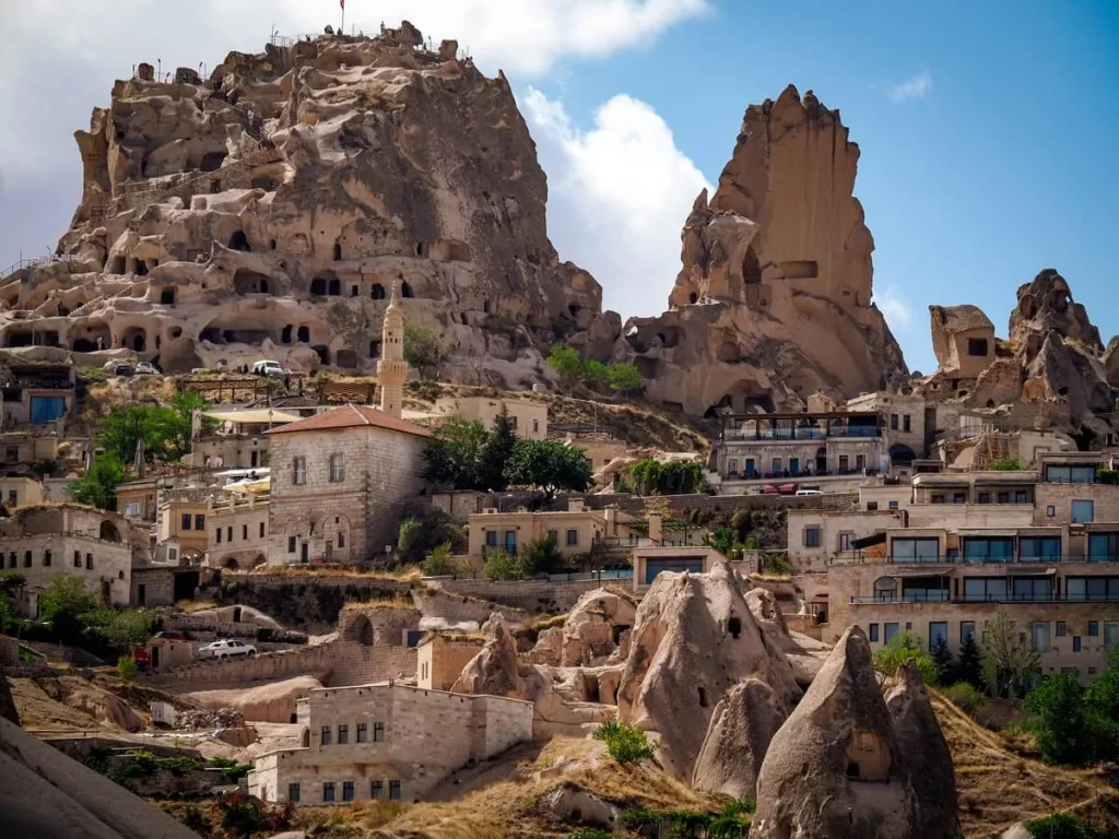 A huge rock castle standing behind a small town with houses and other rock formations in Cappadocia