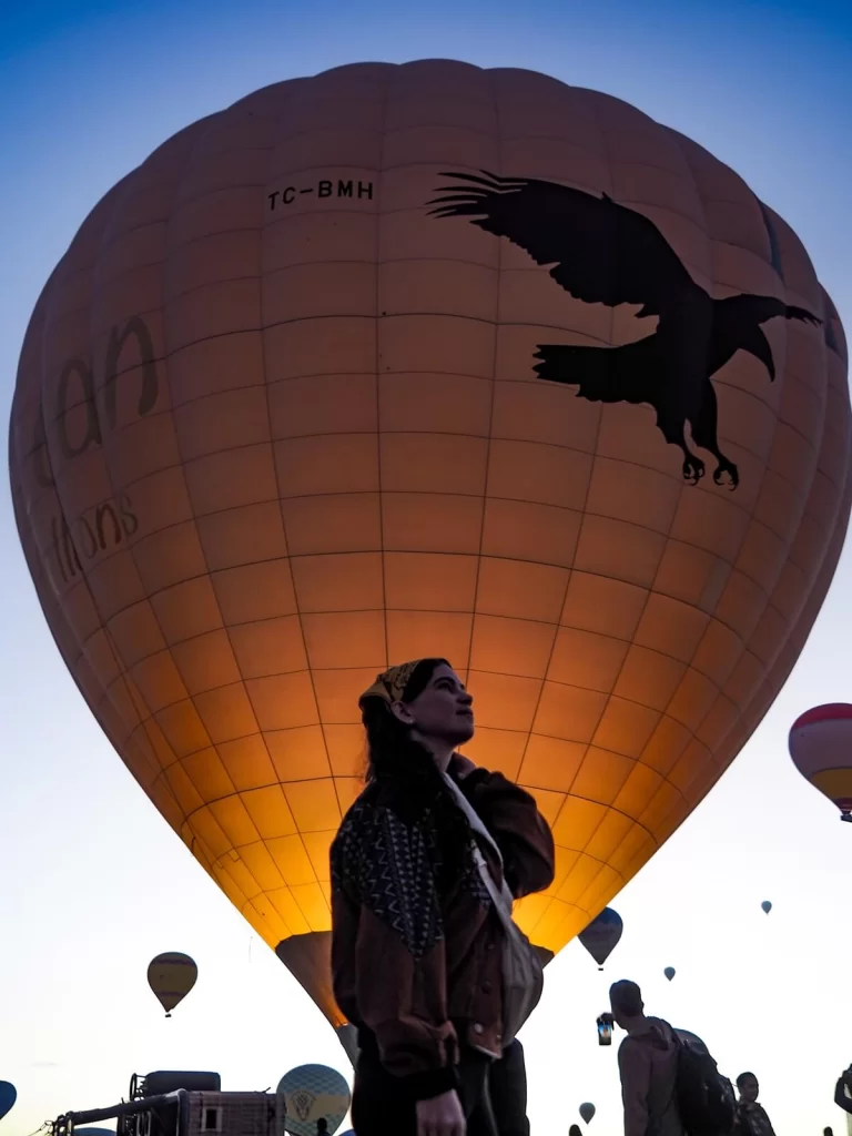 Female Traveller is standing in front of a huge Hot Air Balloon