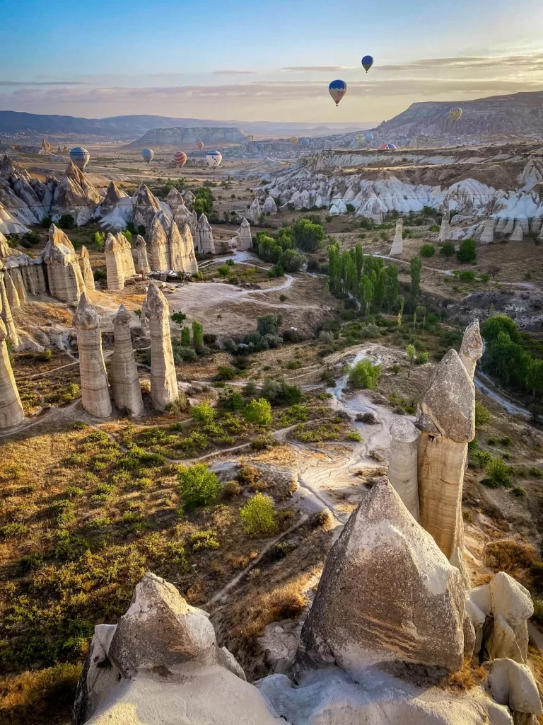 An open valley with huge rock formations and hot air balloons in the sky in Cappadocia Turkey