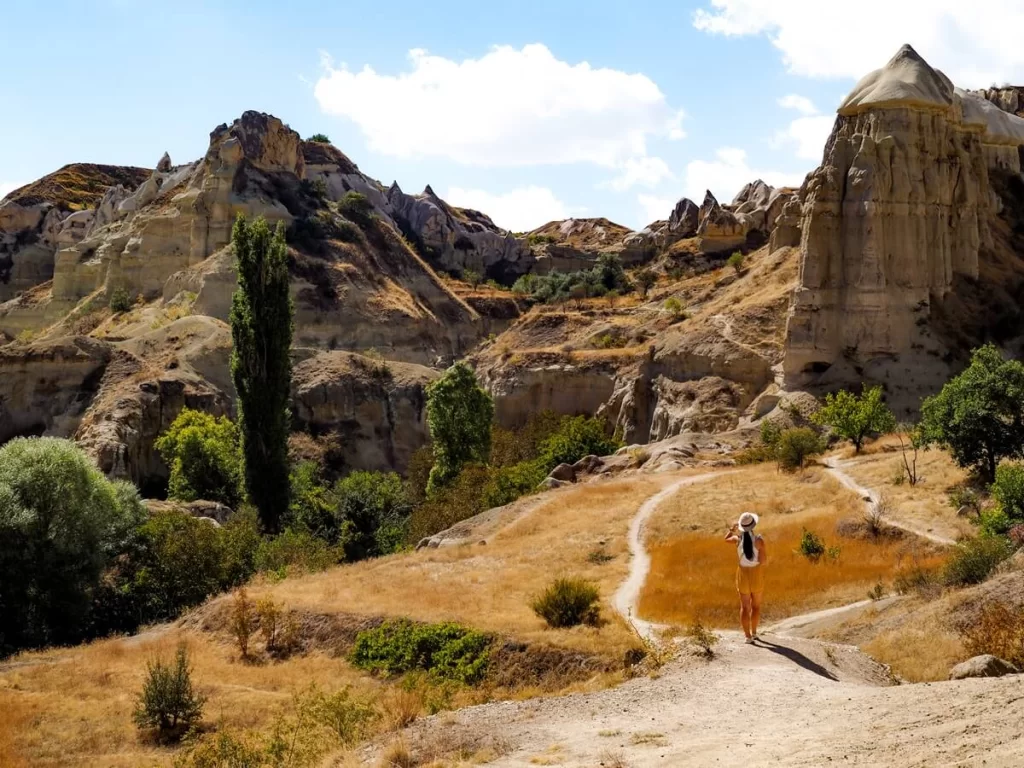 A female hiker is walking along a path surrounded by tall cliffs in Cappadocia