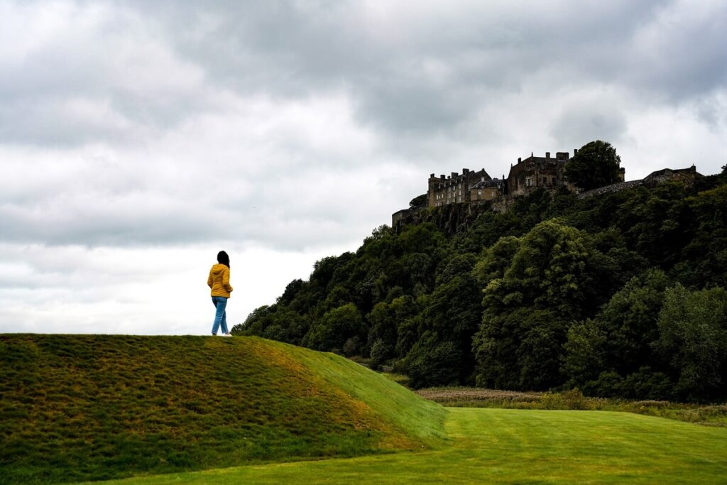 A female is standing on a small hill overlooking Stirling Castle in Scotland