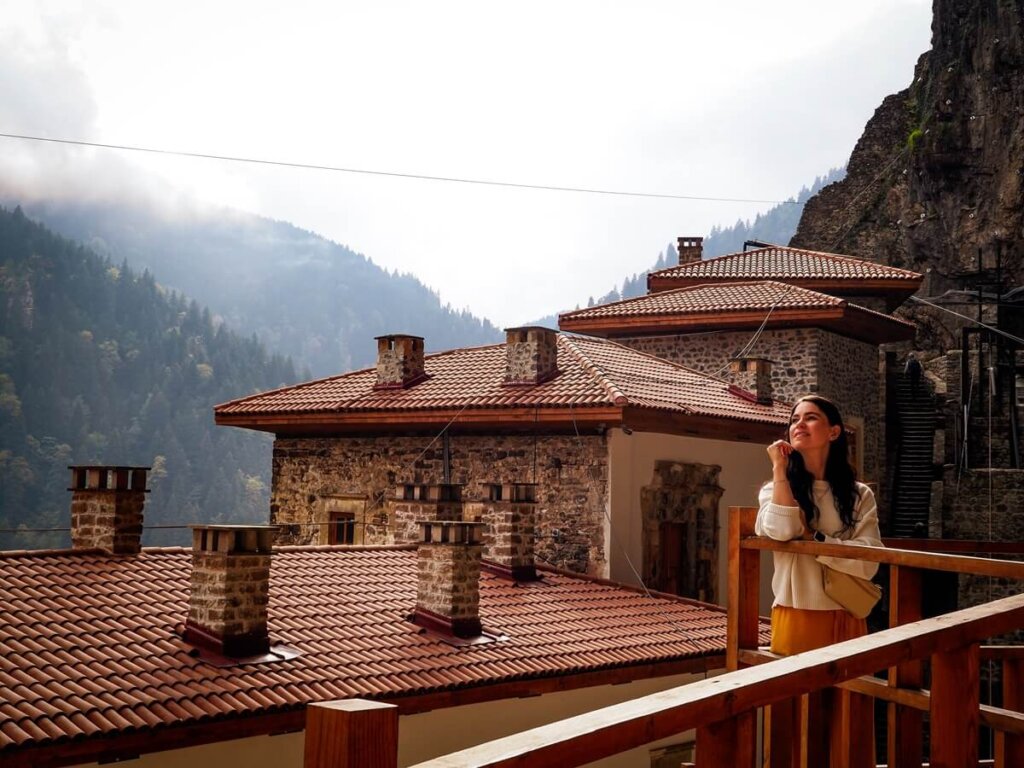 A female traveller is standing on a balcony with old buildings behind her