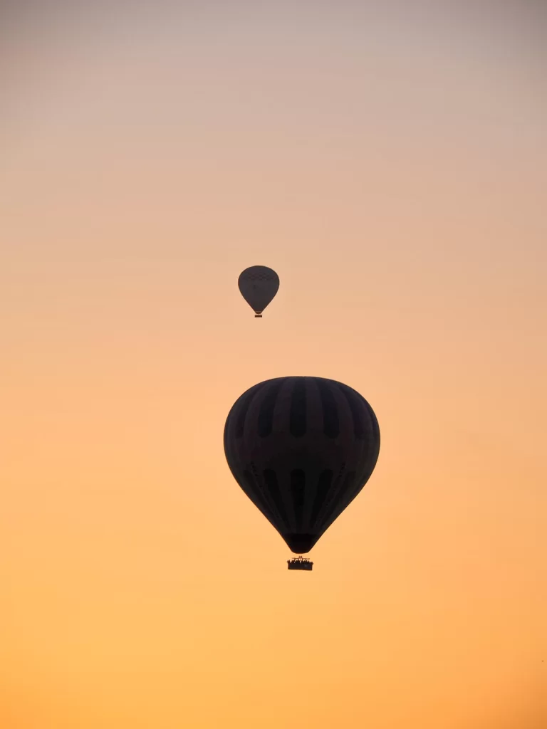 two hot air balloons are in the sky during sunrise