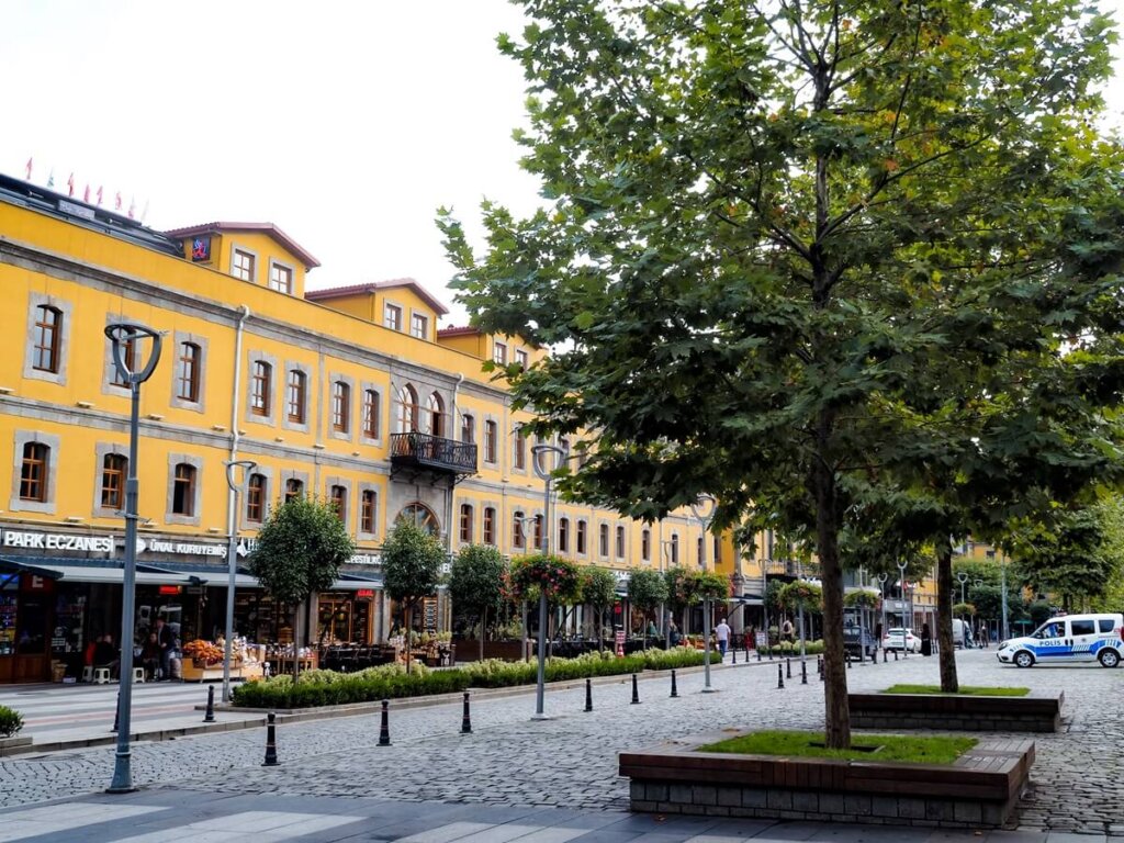 A long yellow building along a cobblestone street with trees