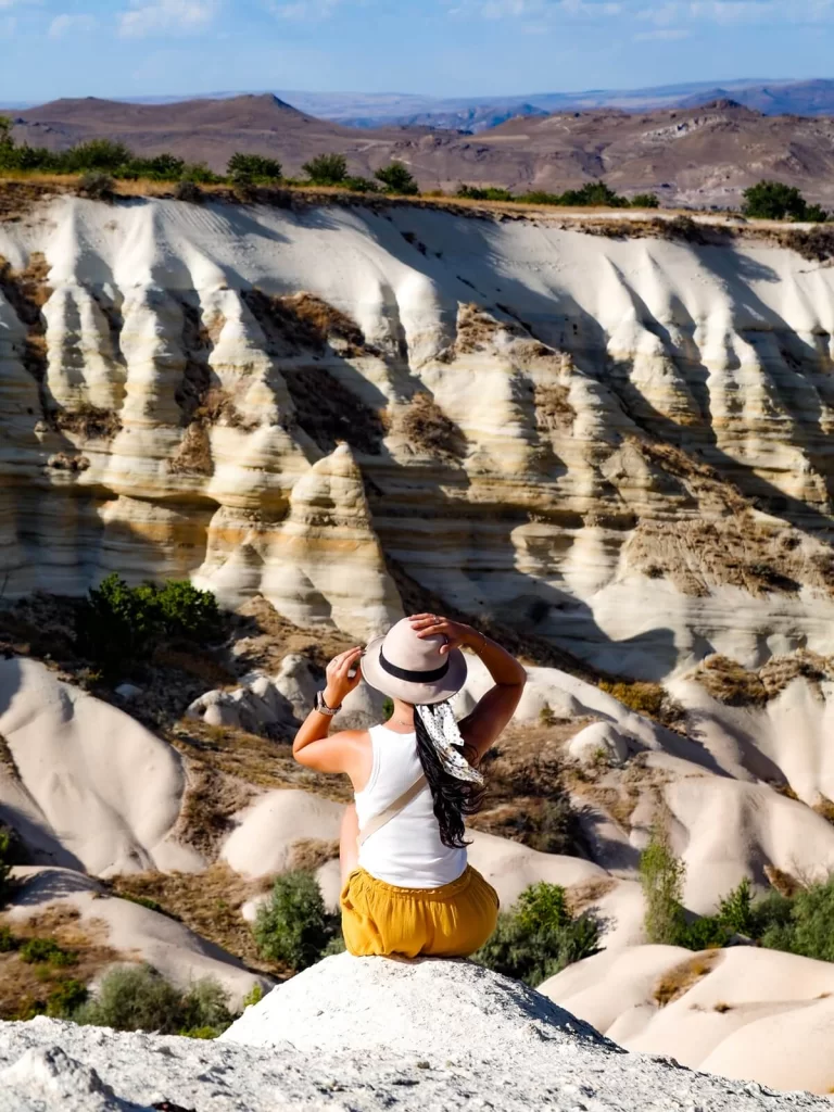 A female traveller is sitting on a rock overlooking the side of a valley