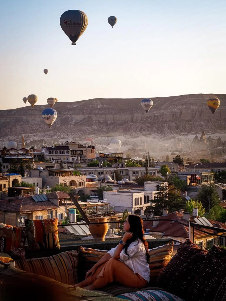 Female traveller is sitting in a balcony if Cappadocia watching the hot air balloons during sunrise