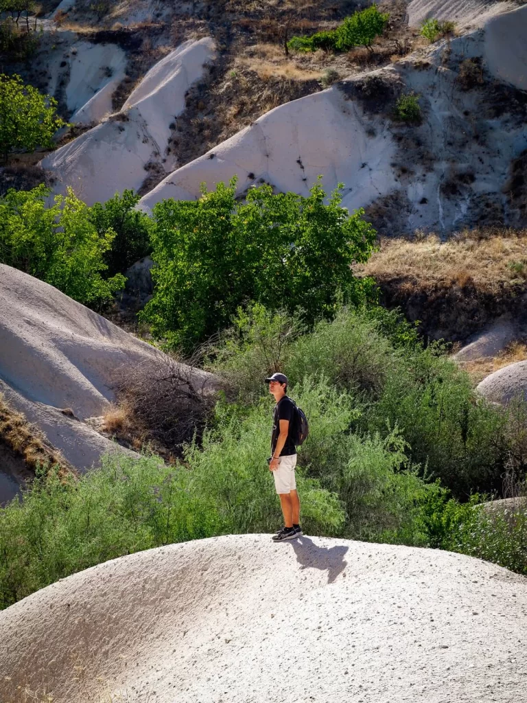 Male hiker is standing on a huge white rock in a valley 
