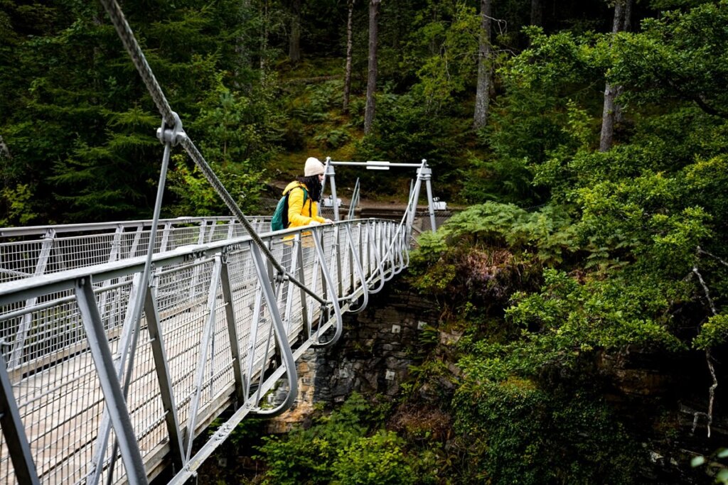 A female is standing on a hanging bridge in Scotland