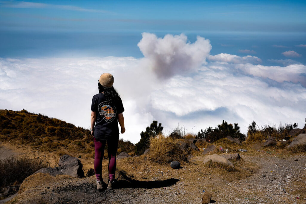 Female hiker is standing on top of Santa Maria Volcano above the clouds