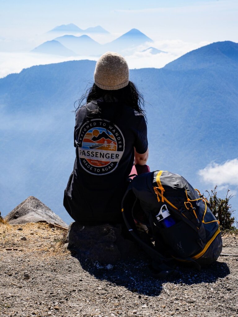 A female hiker is sitting on top of a volcano with her backpack next to her