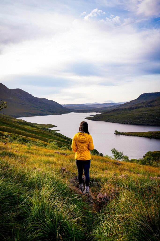 Female hiker is standing in a field overlooking a loch in Scotland