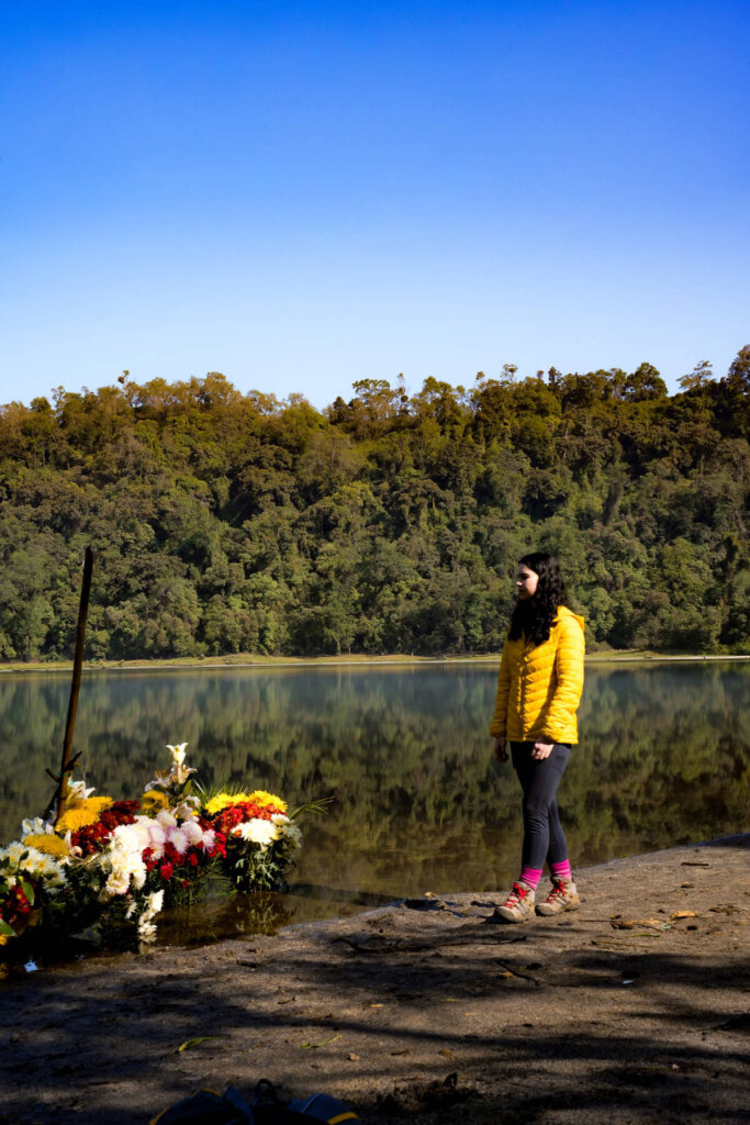 Female is standing next to flower offering at the shores of Laguna Chicabal