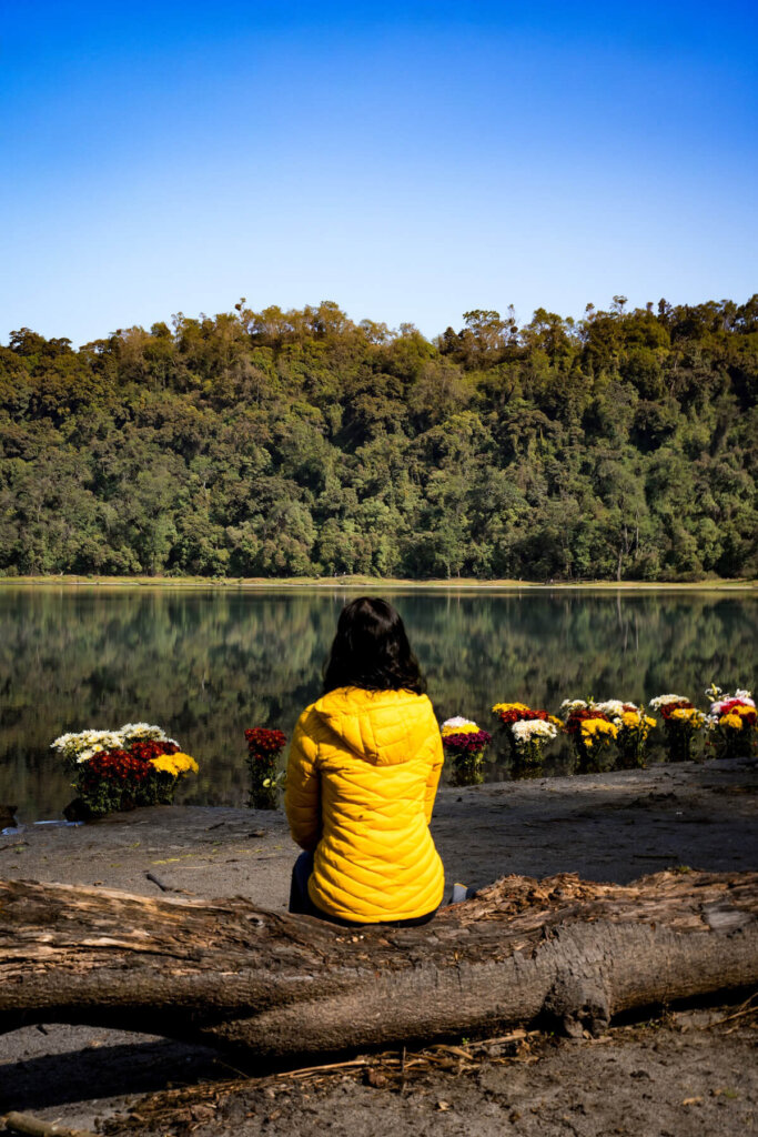 Female in yellow jacket is sitting in front of Laguna Chicabal crater lake near Xela Guatemala