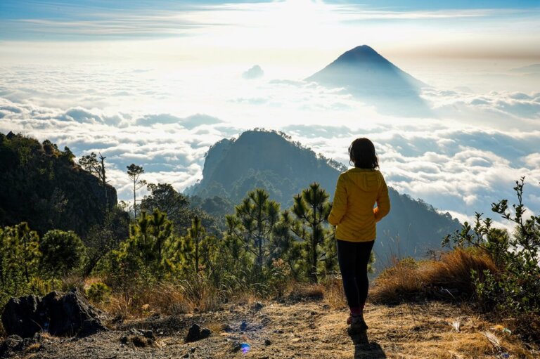 Female is standing on top of a volcano above the clouds during sunrise