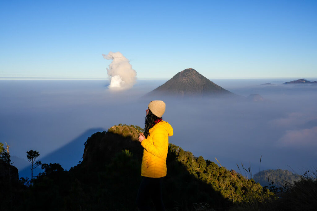 Female hiker is standing in front of a cone shape volcano