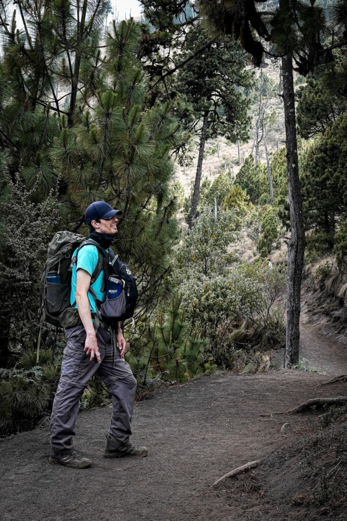 A male hiker is standing on the path wearing a backpack at his front and back