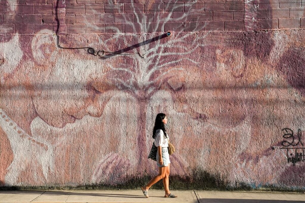 A woman is walking in front of a mural in Tulum Mexico