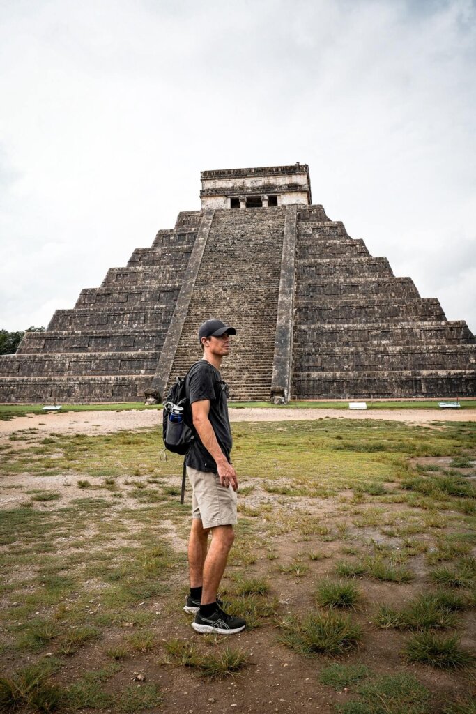A male traveler is standing in front of a pyramid temple in Chichen Itza Mexico