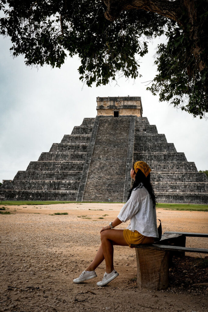 Female traveler is sitting on a bench in front of a temple pyramid in Mexico