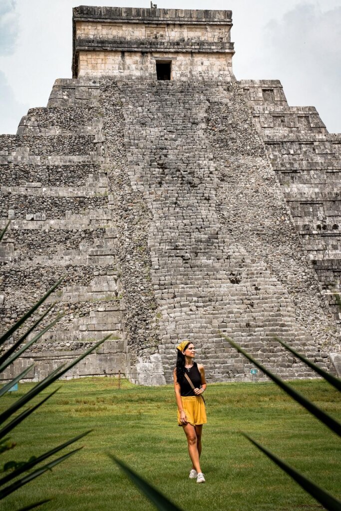 A female traveler is standing in front of a pyramid temple in Chichen Itza Mexico